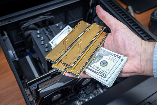 Hand holding gold RAM modules and dollar bills over an open PC case. Concept of rising RAM prices. High-performance computer with expensive components