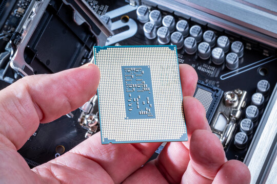 CPU with LGA socket held in technician's hand. Background shows motherboard during PC assembly or upgrade. Visible motherboard components. High-end computer parts