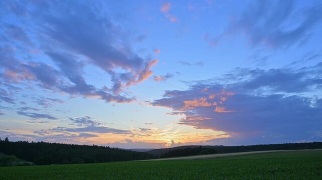 Der Sonnenuntergang taucht den Himmel &uuml;ber einem weiten Feld in warme Oranget&ouml;ne, Wolken ziehen sanft vorbei, Sommer, Gro&szlig;heubach, Miltenberg, Spessart, Bayern, Deutschland