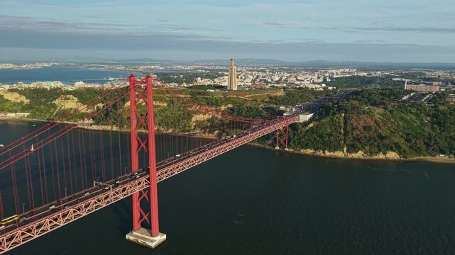 Panoramic aerial view of the 25 de Abril suspension bridge crossing the Tagus River toward Almada, with the Cristo Rei monument and urban landscape in the background.