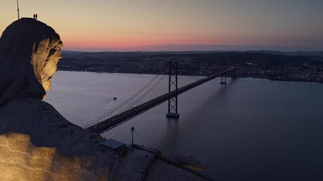 Aerial twilight view of the illuminated Cristo Rei monument overlooking the 25 de Abril suspension bridge and Tagus River between Almada and Lisbon, Portugal.