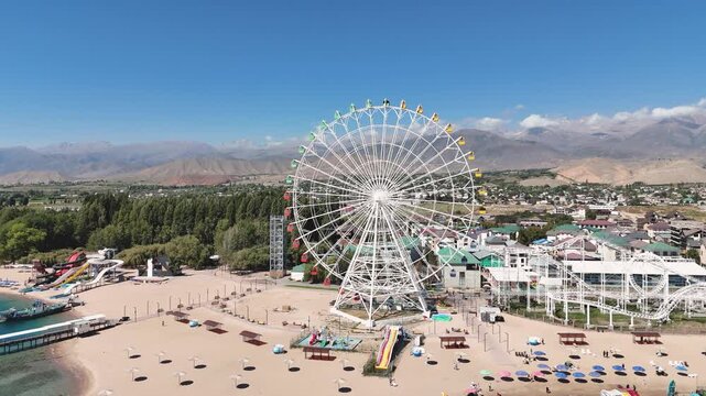 Ferris wheel by Issyk-Kul Lake with scenic mountains in the background, a popular tourist spot.