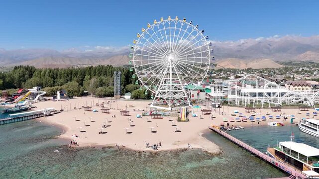 Ferris wheel by Issyk-Kul Lake with scenic mountains in the background, a popular tourist spot.