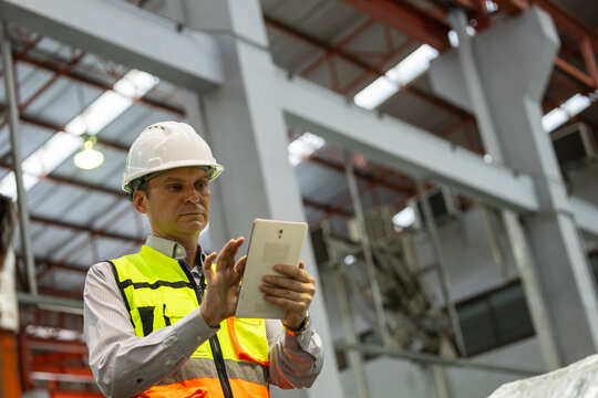QC engineer uses a tablet to inspect a large industrial or logistic warehouse.