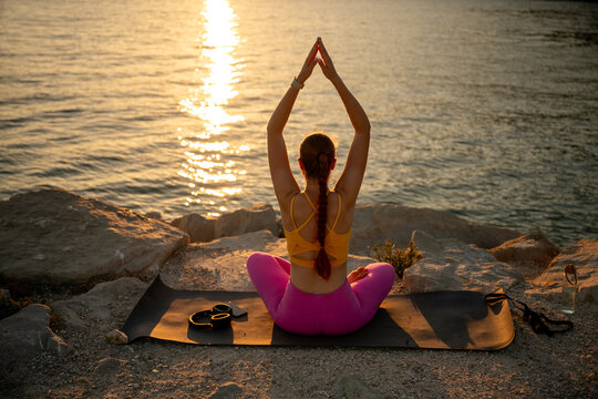 Woman practicing yoga on seaside rocks at sunset