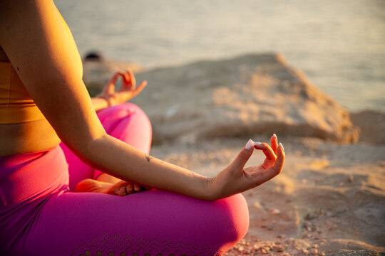 Woman meditating in yoga pose by the sea at sunset