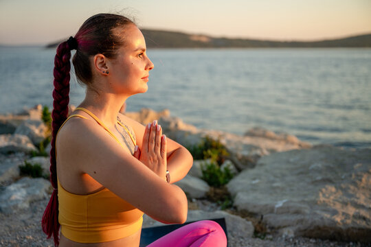 Woman meditating in yoga pose by the sea at sunset