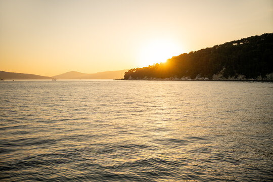 Golden sunset over calm sea by forested coastline