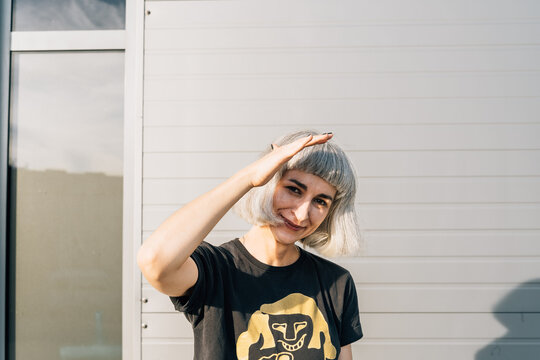 Young woman shading eyes in sunlight against modern wall