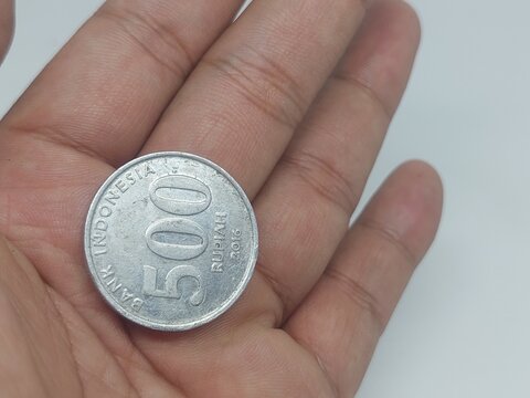 Close-up view of a person holding an Indonesian 500 rupiah coin in open palm. Concept for small investment, micro savings, finance, currency exchange, economy, and paying cash on a isolated white