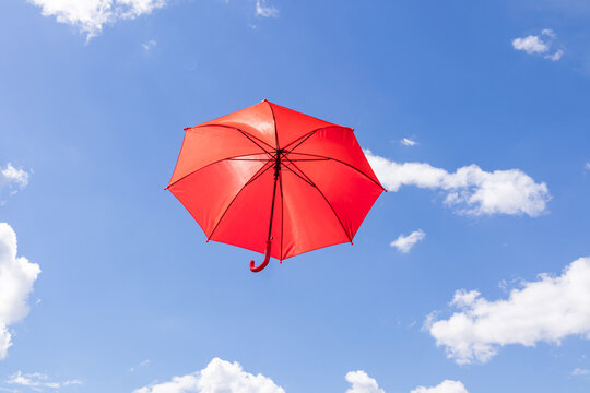 Red umbrella floating in blue sky with white clouds