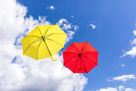 Colorful umbrellas floating in blue sky with clouds