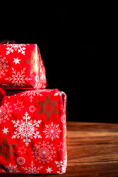 Wrapped Christmas gift boxes with red snowflake paper on a wooden surface against black background