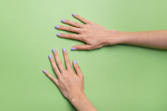 Caucasian woman hands with lavender nail polish on green