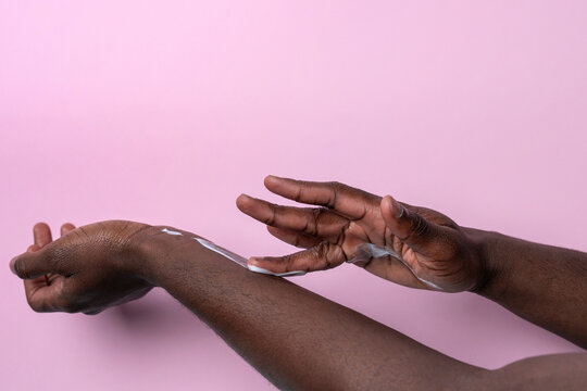 Hands applying moisturizing lotion on forearm on pink