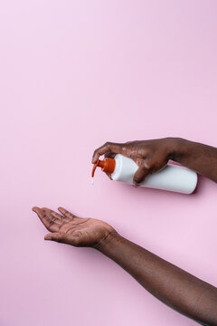Black mans hands applying soap from pump bottle on pink