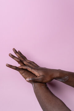 Black man hands applying moisturizer on pink background