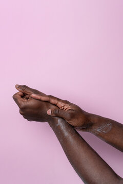 Black man hands applying lotion on wrist on pink background