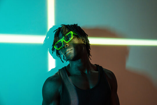 African man in neon glasses posing in colored studio light