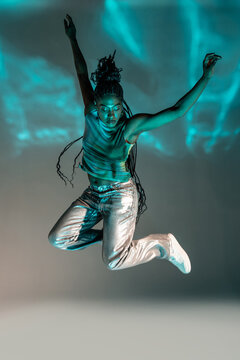 Afro woman dancer jumping with braids in teal light