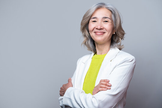 Smiling senior Asian woman in white blazer, gray background