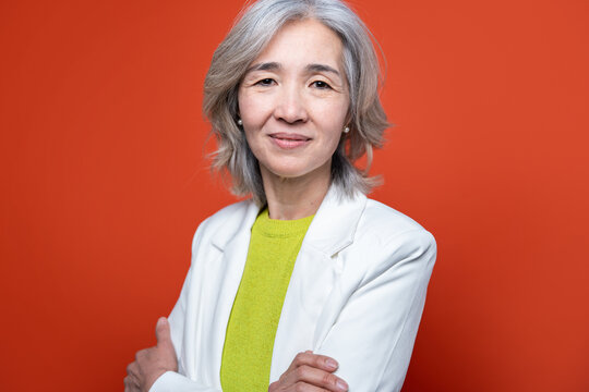 Senior Asian woman portrait in white blazer on orange background