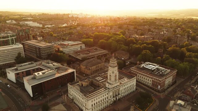Drone shot tracking west over Barnsley cityscape into golden hour sunset backlit town hall, UK.