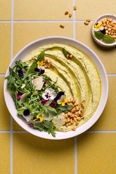 Savory pesto hummus with salad and pine nuts on plate