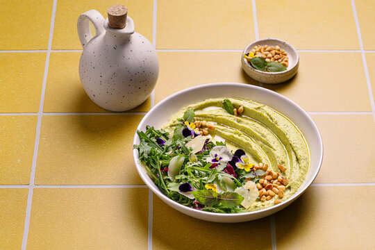Pesto hummus with basil and pine nuts on yellow tiles