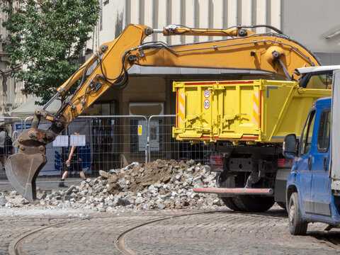 A yellow hydraulic excavator next to a large, yellow RORO (Roll-On/Roll-Off) skip container. commercial waste removal services. A blue truck  for hauling away the debris. Demolition operations. 