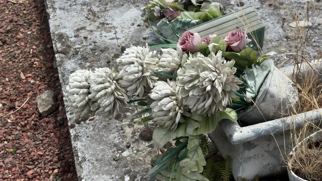 Faded artificial flowers on weathered grave in cemetery
