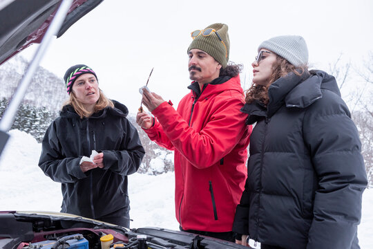 Friends checking car engine in snowy winter setting