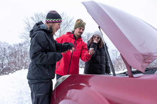 Friends checking car under the hood in winter