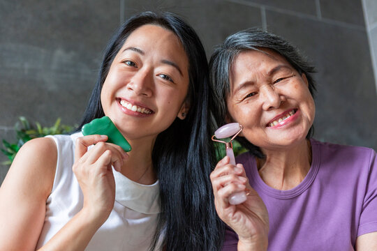 Smiling mother and daughter using facial roller and gua sha
