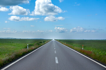 Obraz premium Straight highway stretching across vast Hokkaido grassland under blue sky and white clouds