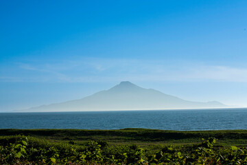 Fototapeta premium Majestic view of Rishiri Island rising from blue sea, seen from Hokkaido coast