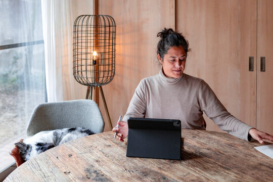 Woman working from home at wooden table with tablet and dog