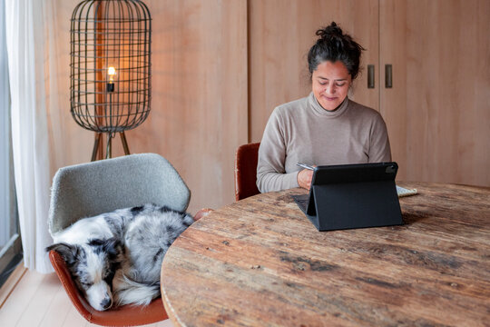 Woman working on tablet at home with sleeping dog nearby