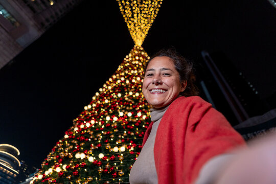 Smiling woman taking a selfie by a lit Christmas tree in China