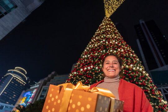 Smiling woman with gift box by giant Christmas tree