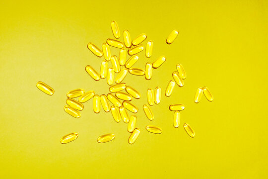 Softgel capsules scattered on a yellow background