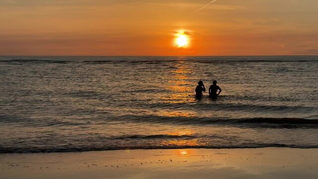 Two people swimming in ocean at golden sunset