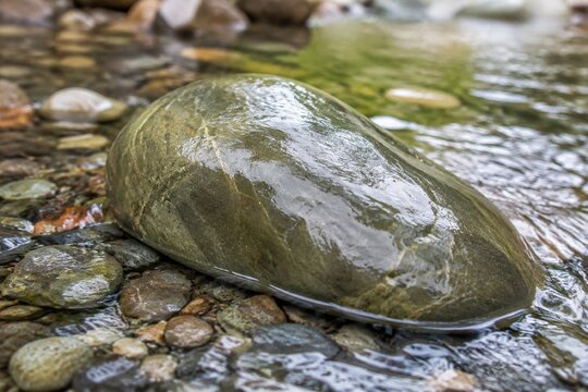 A polished soapstone rock in a clear stream with water flowing over it.