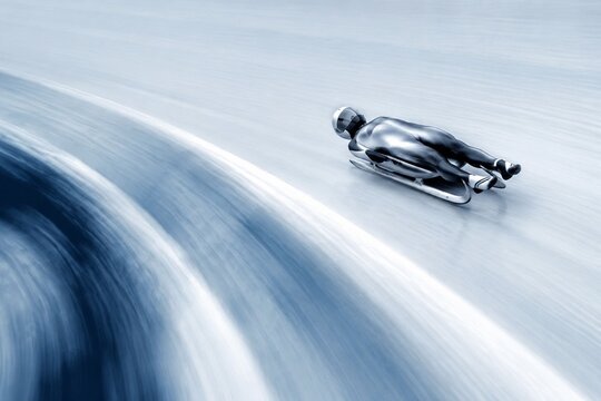 A silver luge sled in motion blur, creating a curved trail on smooth ice.