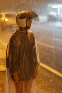 Woman in rain poncho and helmet at night in tropical rain