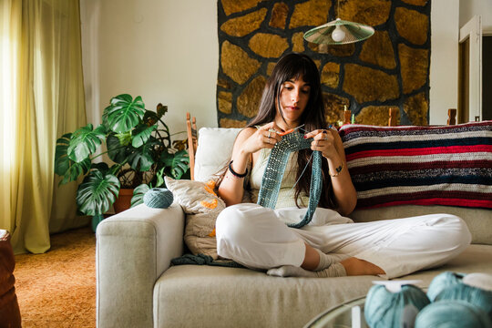 Woman knitting on sofa in cozy living room at home