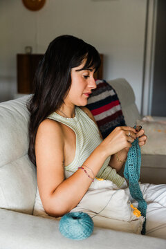 Young woman knitting on sofa at home with yarn and needles
