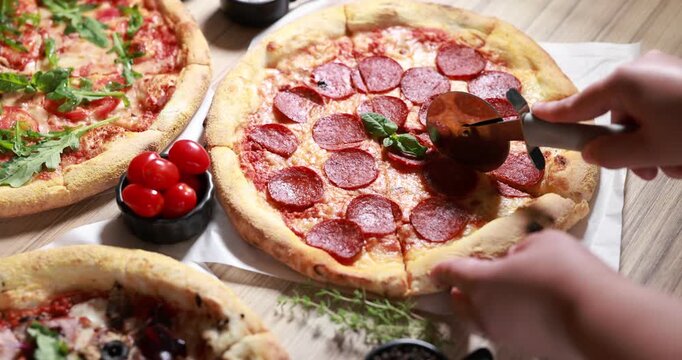 Woman cutting tasty pizza with salami at wooden table, closeup