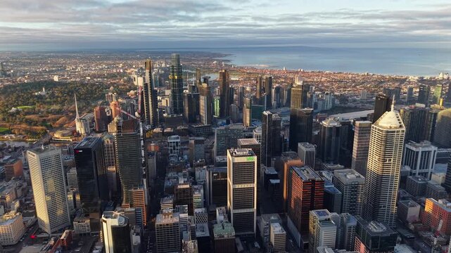 Aerial drone video of Melbourne CBD and Southbank at sunrise, shot from further north, showing skyscrapers, Albert Park Lake, Port Phillip Bay and warm city light
