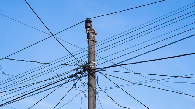 Utility pole with multiple overhead power lines under a bright blue sky, representing electricity distribution, communication networks, and urban infrastructure.